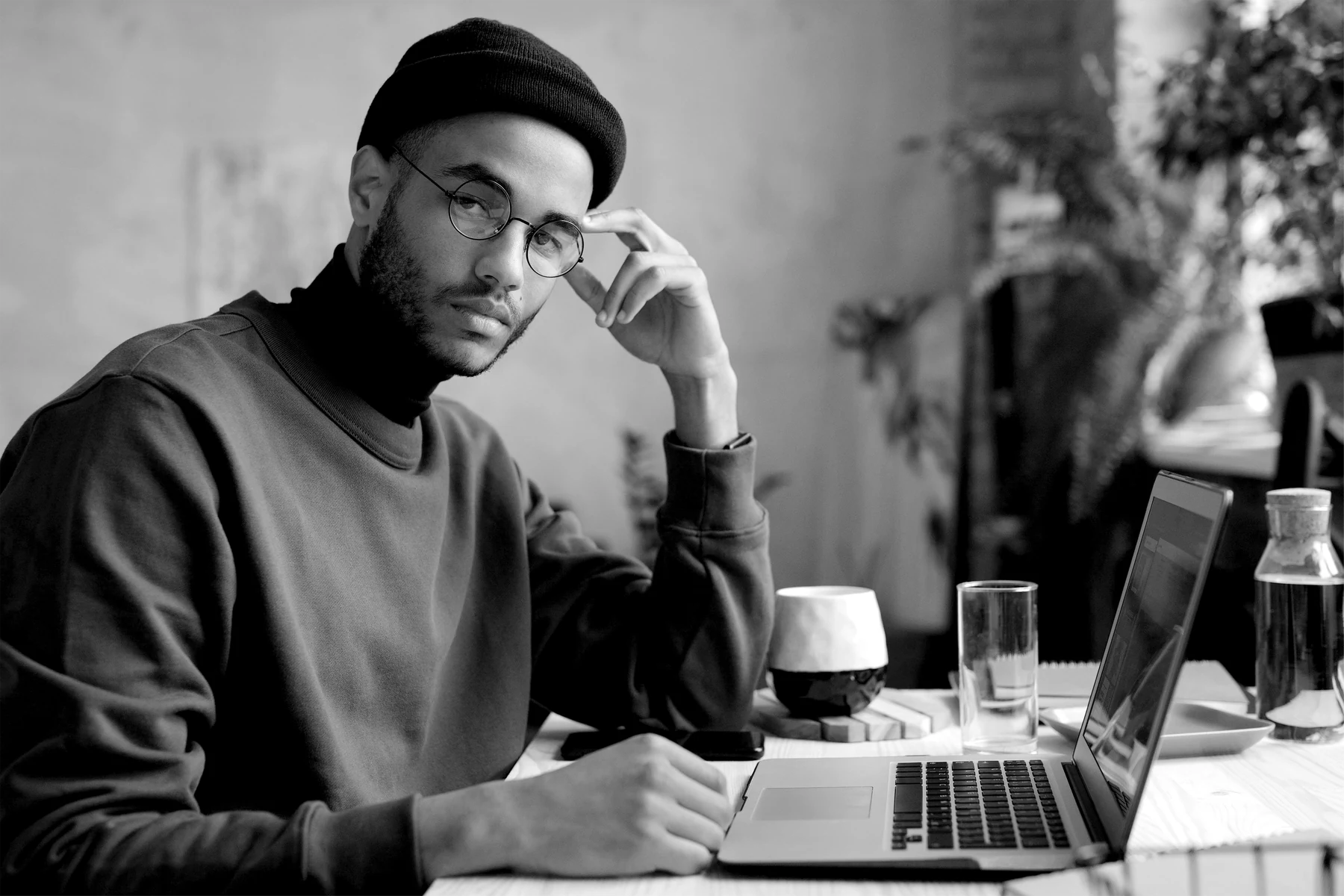 A person in a beanie and glasses working at a laptop